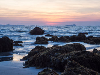 Rocks on beach against sky during sunset