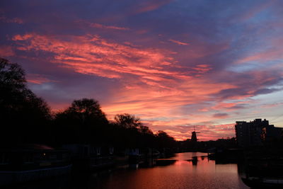 Silhouette trees by canal against sky during sunset