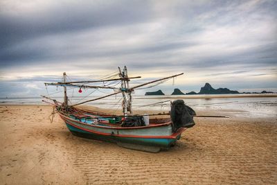 Boat moored on beach against sky during sunset