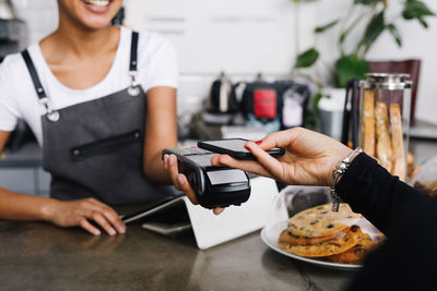 Cropped hand of customer using mobile phone for contactless payment to owner at cafe