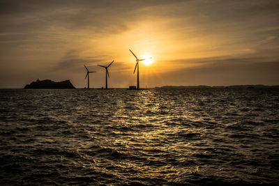 Silhouette of wind turbines on sea at sunset