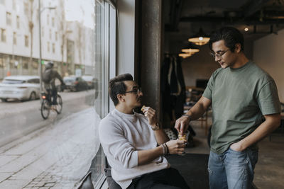 Businessman talking with male colleague while having cookie in break at startup company