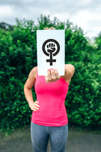 Women covering face with placard while standing against plant