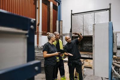 Mature worker gesturing while talking with male and female coworker in steel industry