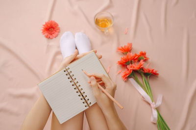 Low section of woman writing in diary while sitting on bed
