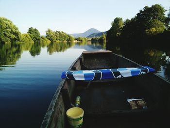 Wooden boat on lake by trees and mountains against clear sky