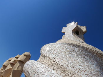 Low angle view of sculpture against building against clear blue sky