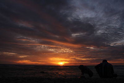 Silhouette people on shore against sky during sunset