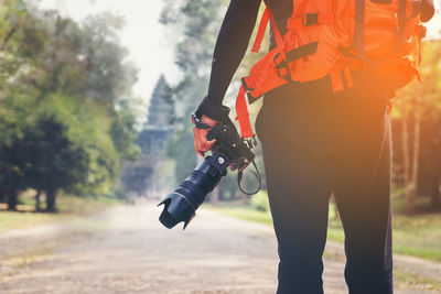 Midsection of man with camera standing against trees