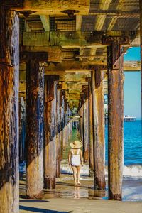 Rear view of woman standing at beach against blue sky