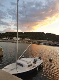 Sailboats moored at harbor against sky during sunset