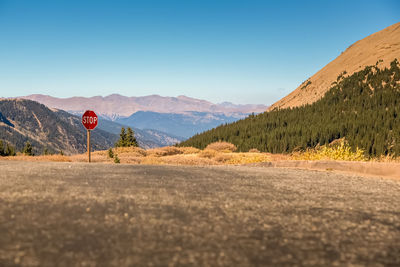 Road leading towards mountains against clear blue sky