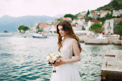 Young woman standing by railing against blue sky