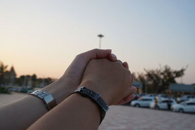 Close-up of hand holding hands against sky at sunset