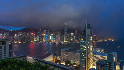 Illuminated city by sea against sky at night