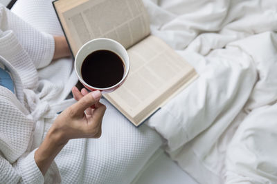 Low section of woman holding coffee cup on bed