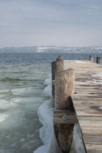 Wooden posts in sea against sky during winter