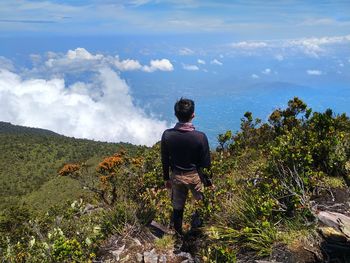 Rear view of man standing on mountain against sky