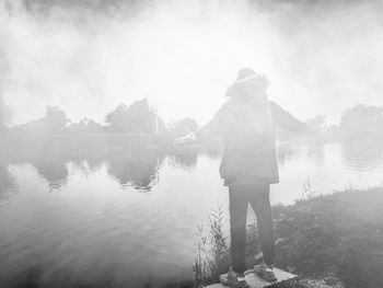 Rear view of man standing by lake against sky