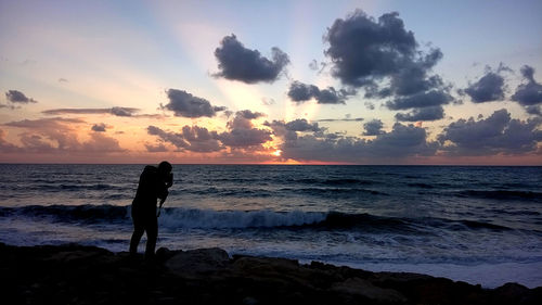 Silhouette people looking at sea against sky during sunset