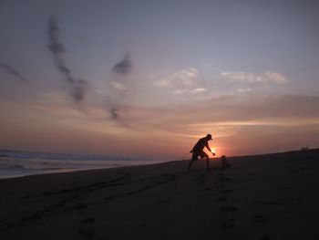 Silhouette person on beach against sky during sunset