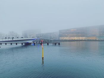 Bridge over river by buildings in city against sky