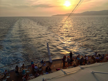 People at sea shore against sky during sunset