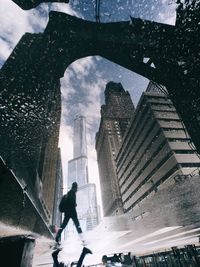 Reflection of man walking by buildings seen in puddle