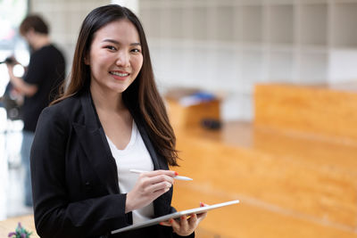 Portrait of young businesswoman using digital tablet while standing in cafe