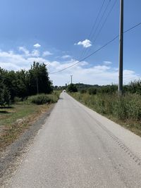 Road by electricity pylon against sky