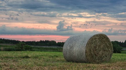 Hay bales on field against sky during sunset