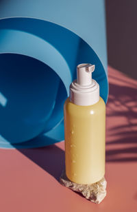 Yellow bottle with a dispenser on a stone on a pink background.