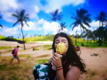 Young woman eating pineapple while standing on field