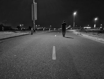 Rear view of man walking on illuminated street at night