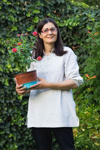 Portrait of woman holding potted plant while standing against plants