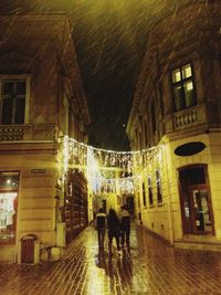 Rear view of people walking on street amidst buildings at night