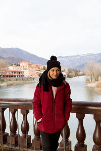 Portrait of young woman standing on railing against lake