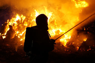 Silhouette firefighter against fire at night