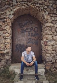 Full length of man sitting against brick wall