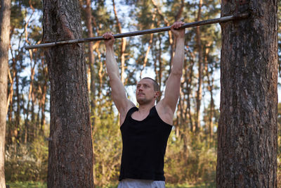 Portrait of man standing by tree trunk in forest
