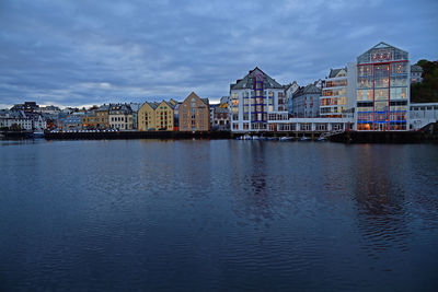 Buildings at waterfront against cloudy sky