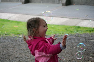 Side view of cheerful girl playing with bubbles in park