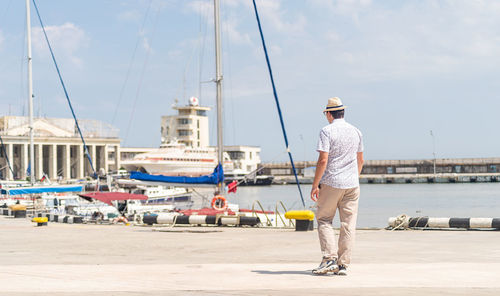 Summer travel. male tourist in straw hat walking in the sea port, boats and yachts on the background