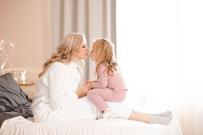 Side view of mother and daughter on bed at home
