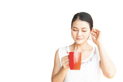 Portrait of a beautiful young woman drinking glass against white background