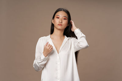 Portrait of young woman standing against brown background