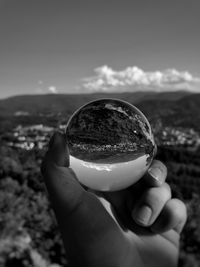 Cropped hand holding crystal ball against sky