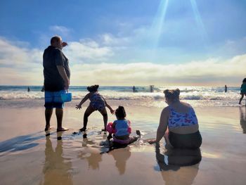 Rear view of people at beach against sky