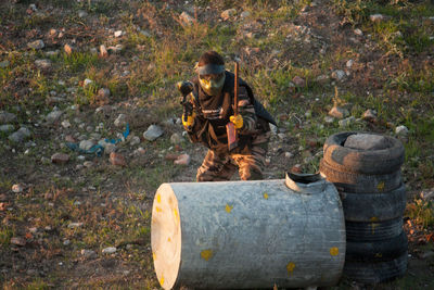 Army soldier hiding behind drum and tire