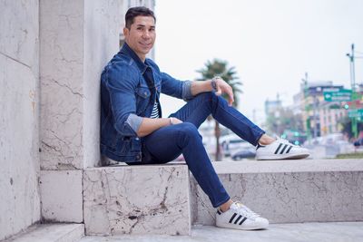 Portrait of young man sitting on sidewalk in city